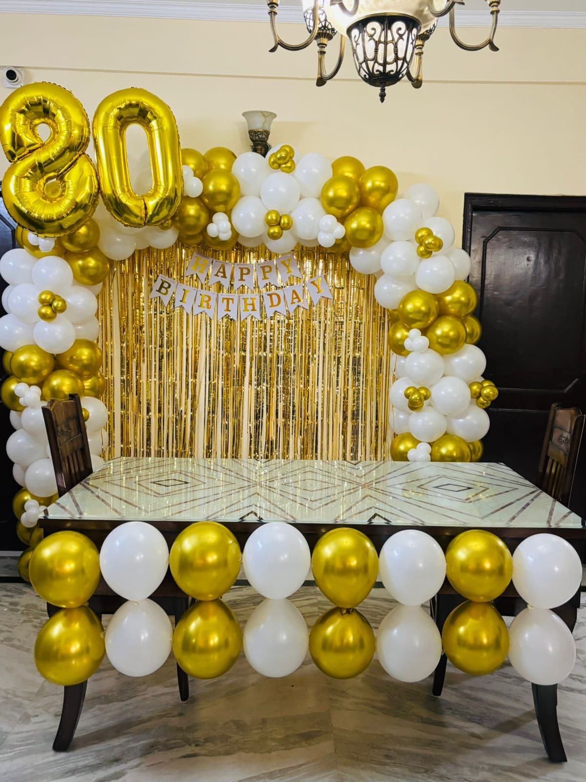 Gold and white 80th birthday setup with a shimmer curtain and number balloons