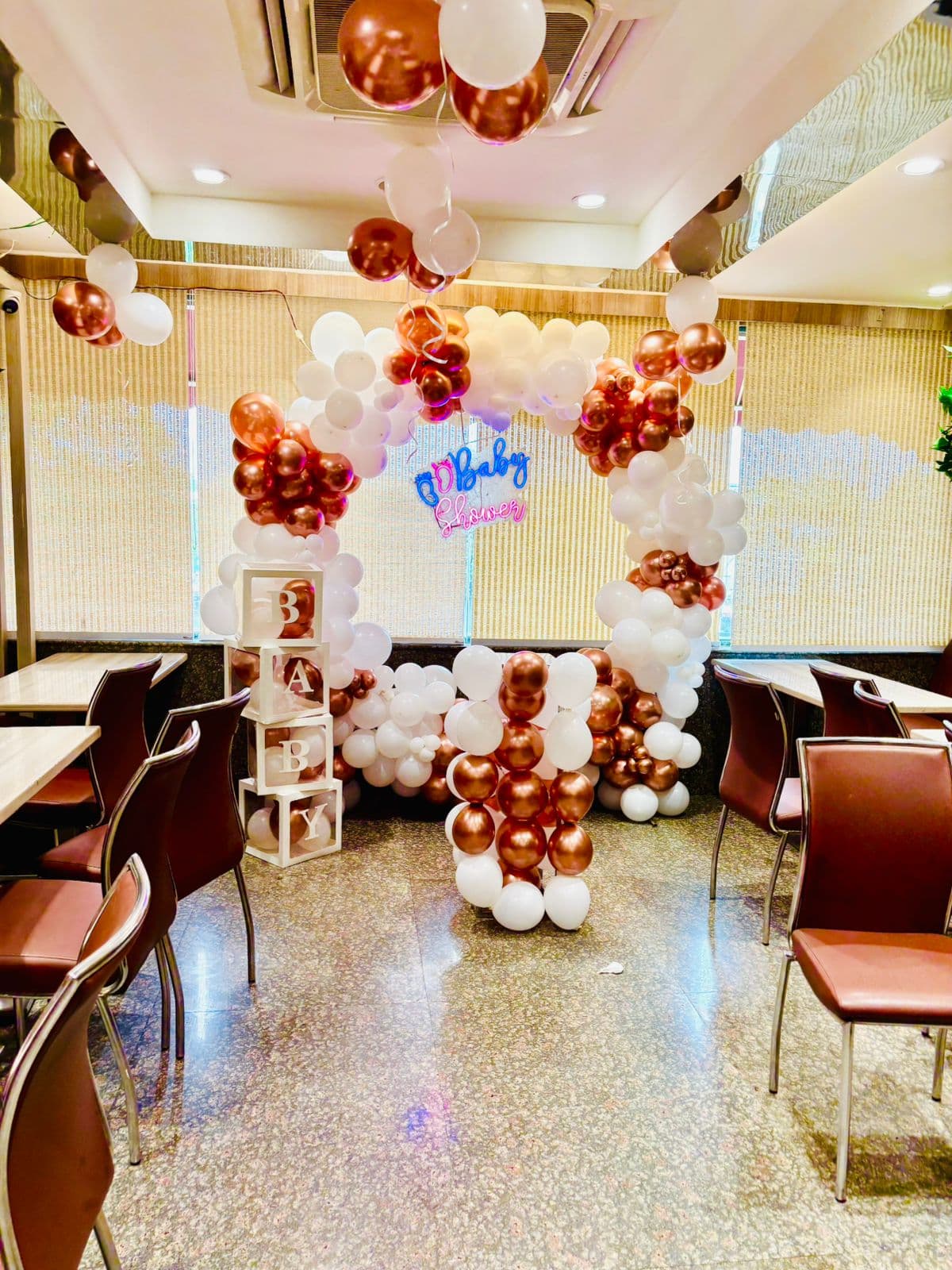 Rose-gold and white baby shower arch with stacked 'BABY' blocks