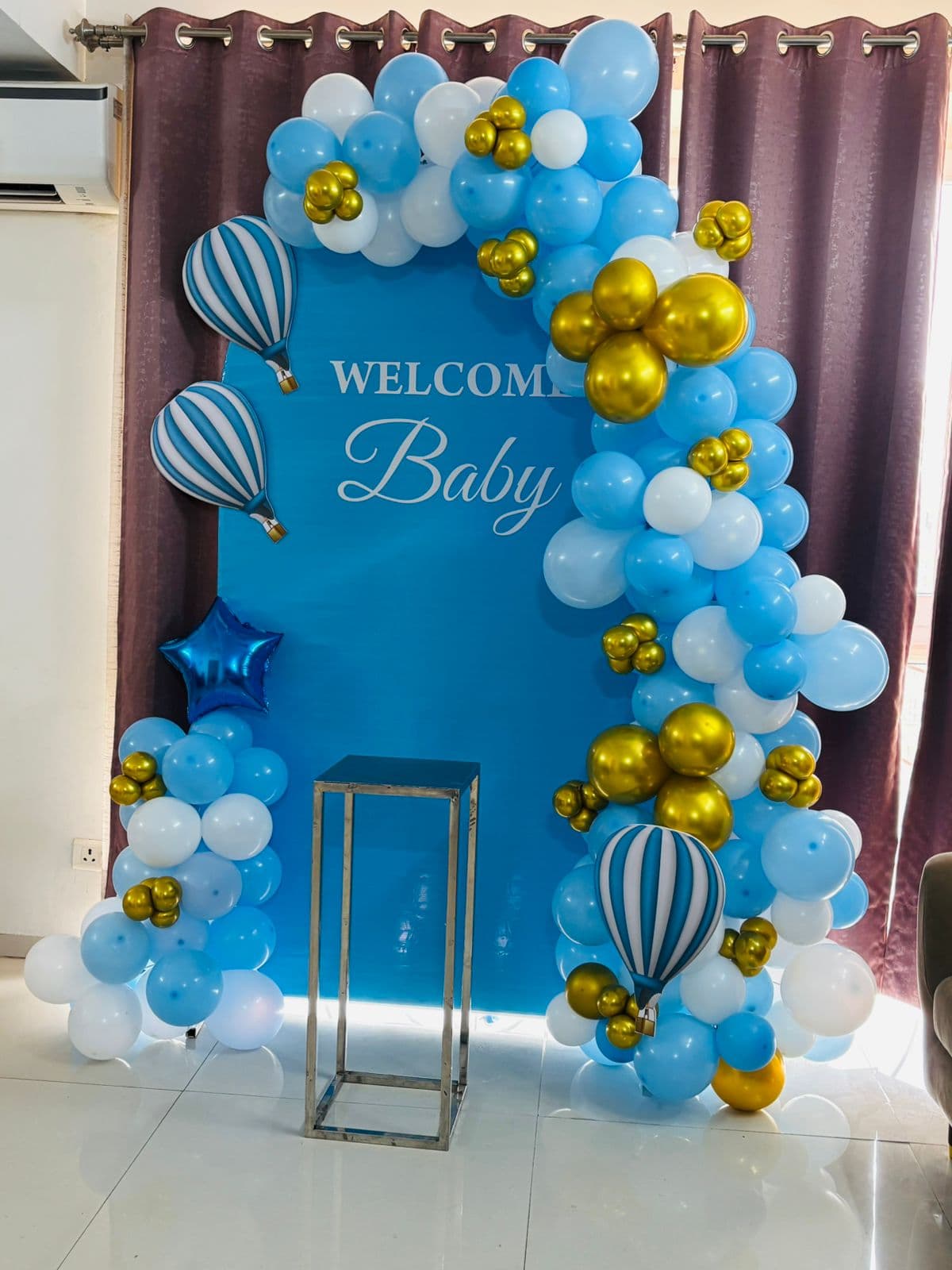 Blue, white and gold 'Welcome Baby' backdrop with hot-air-balloon props